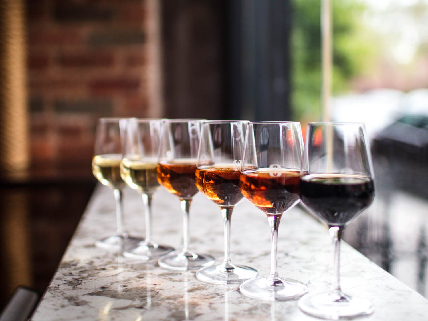 A diagonal line of wineglasses containing a range of sherries, from light to dark, on a marble countertop