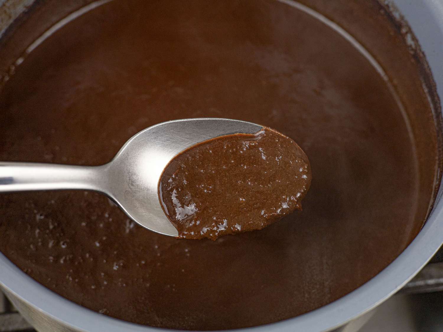 Spoon lifting pork blood sauce out of saucepan to illustrate texture