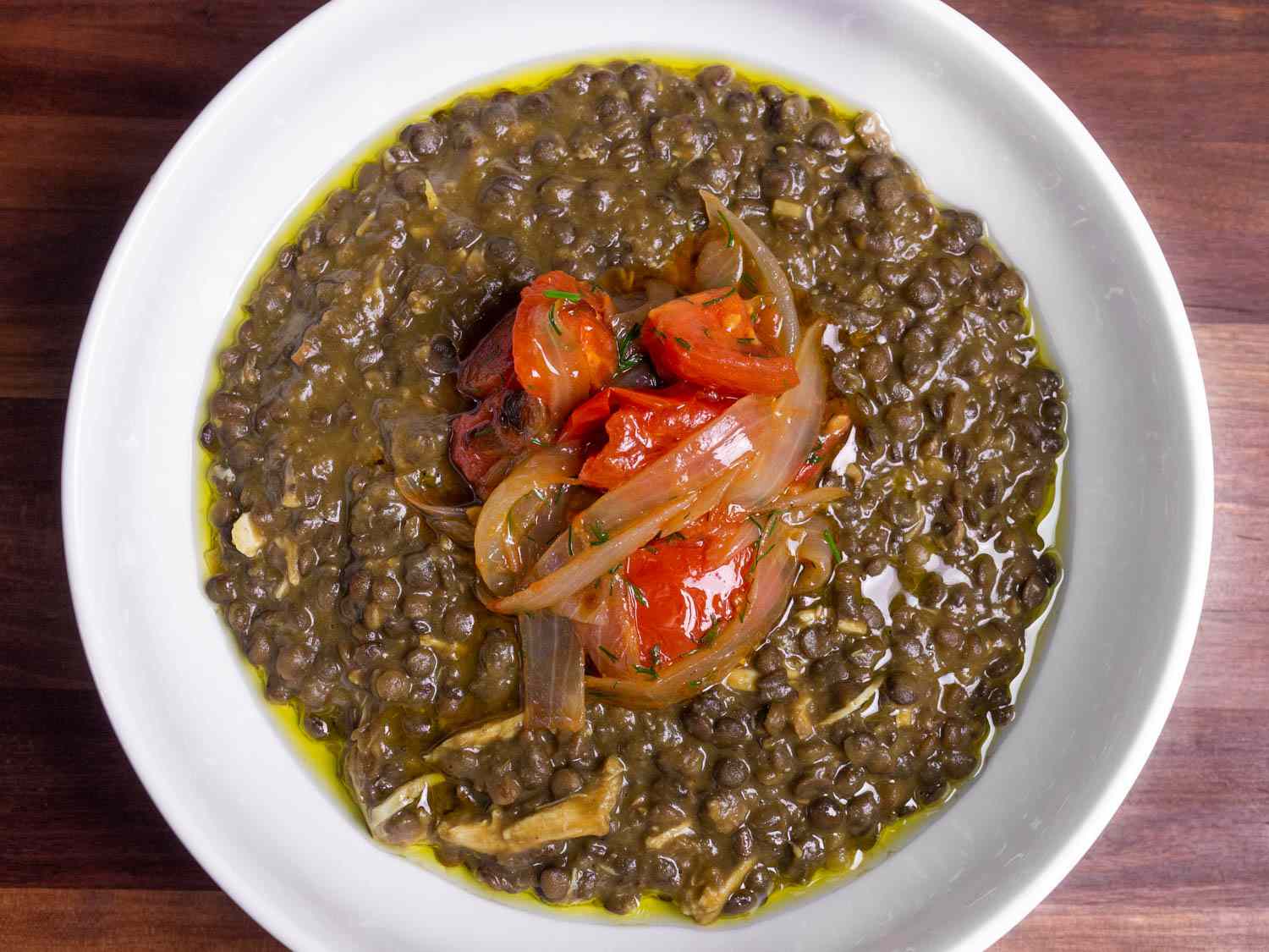 Overhead shot of a bowl of chicken and lentil stew topped with fried onions and tomatoes.