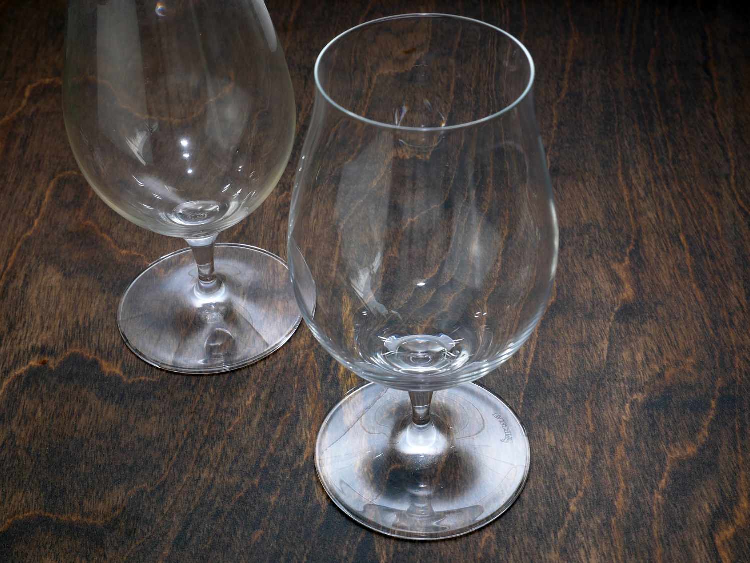 two tulip beer glasses on a dark wood surface