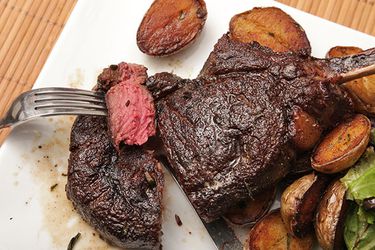 A forkful of medium rare meat cut from a butter-basted bison rib steak plated with crispy potatoes