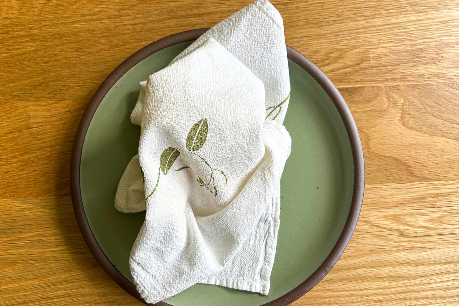 A folded cloth napkin with a leaf design on a green plate