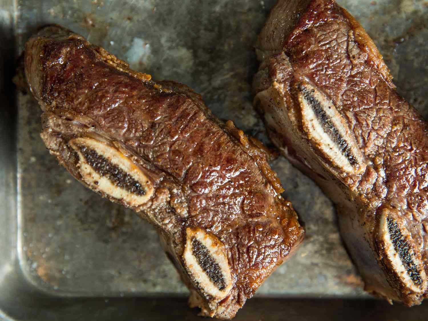 Two slaps of browned bone-in beef short ribs on a baking sheet.