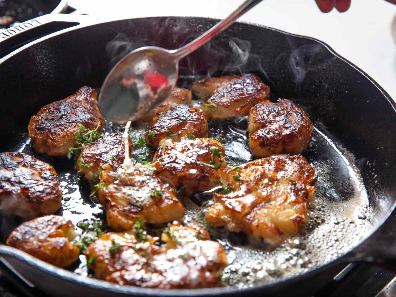 Smashed sunchokes cooking in a cast iron skillet. A spoon is basting the fat on the sunchokes.