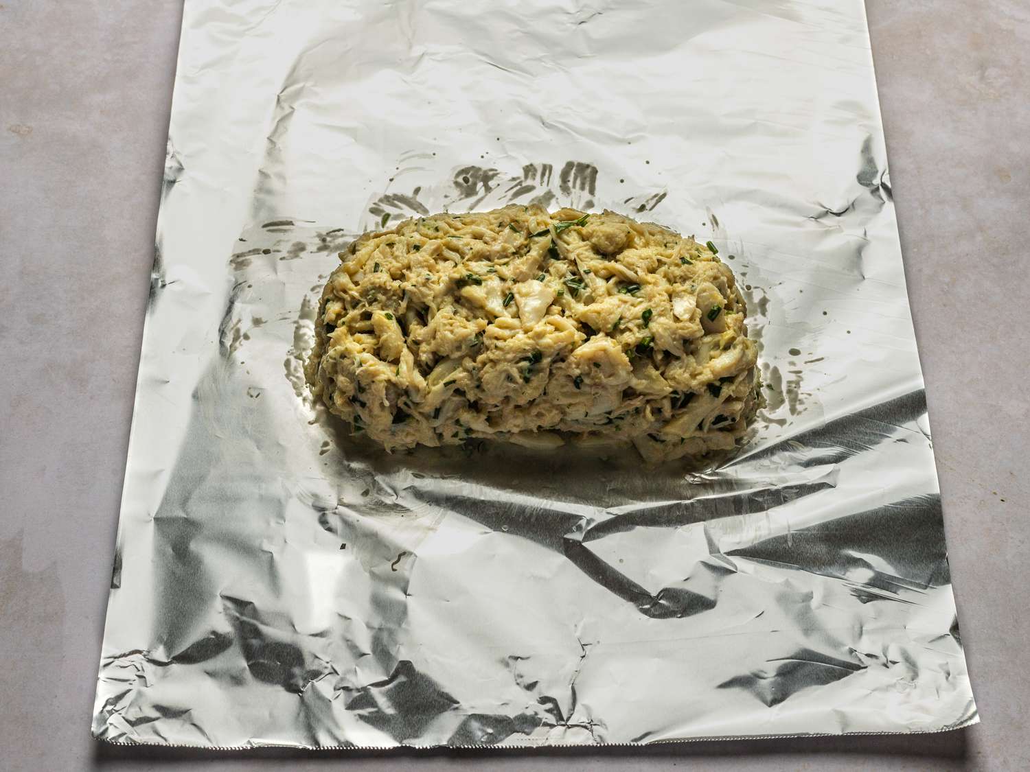 Crab mixture formed into a rough log about 6-inches wide on a sheet of aluminum foil.