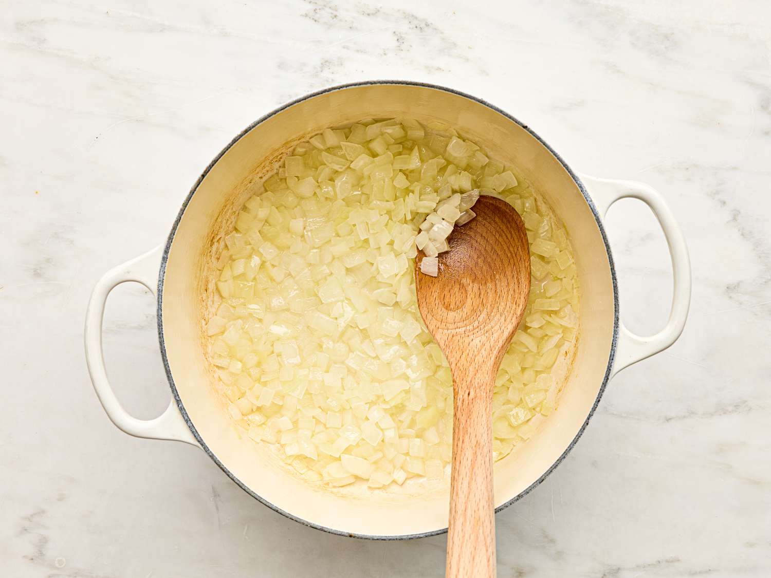 Cooking diced onions in a pot with a wooden spoon