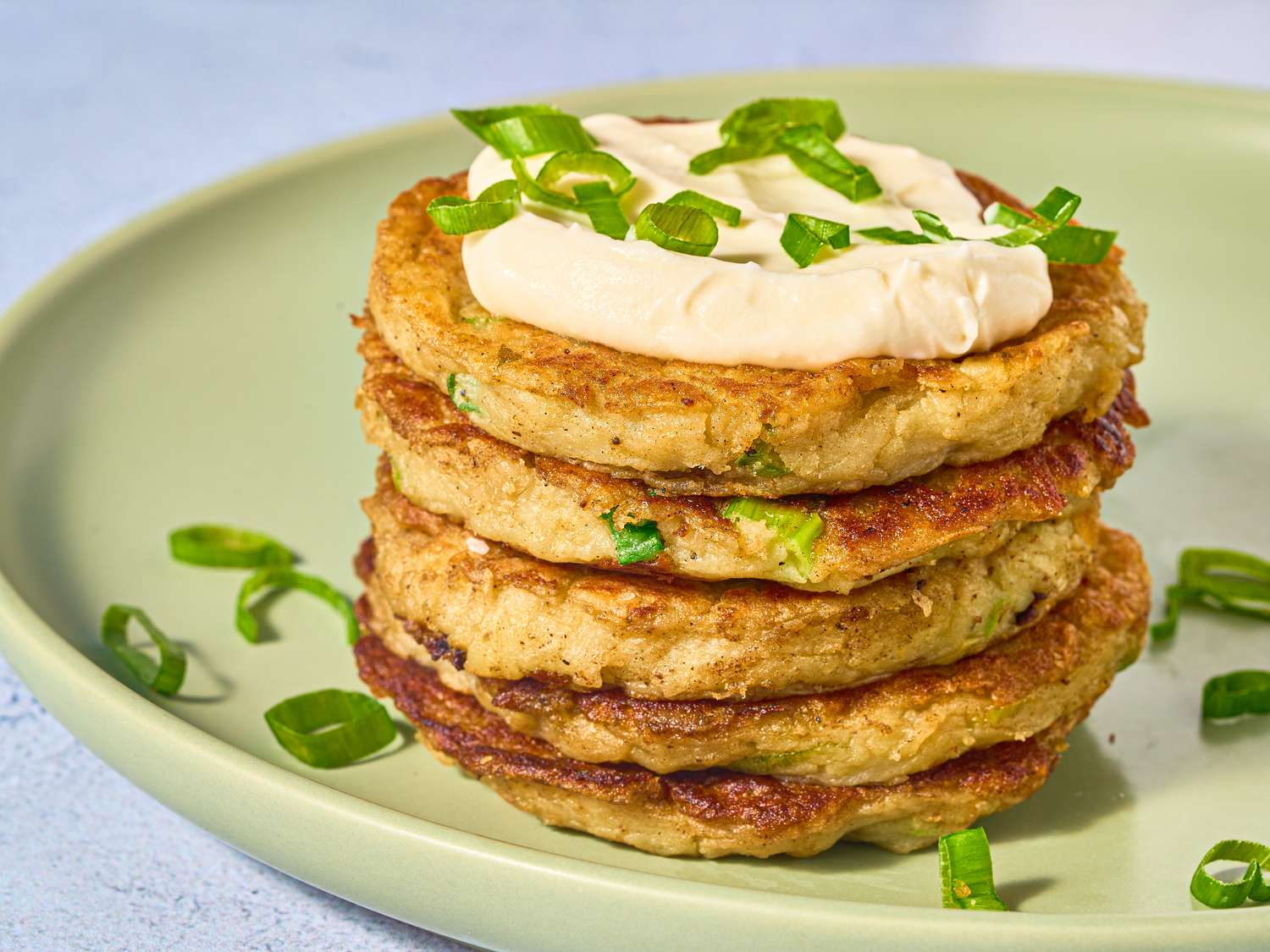 stack of boxty pancakes with dollop on sourcream, and garnished with green onions on a green place on stone surface.