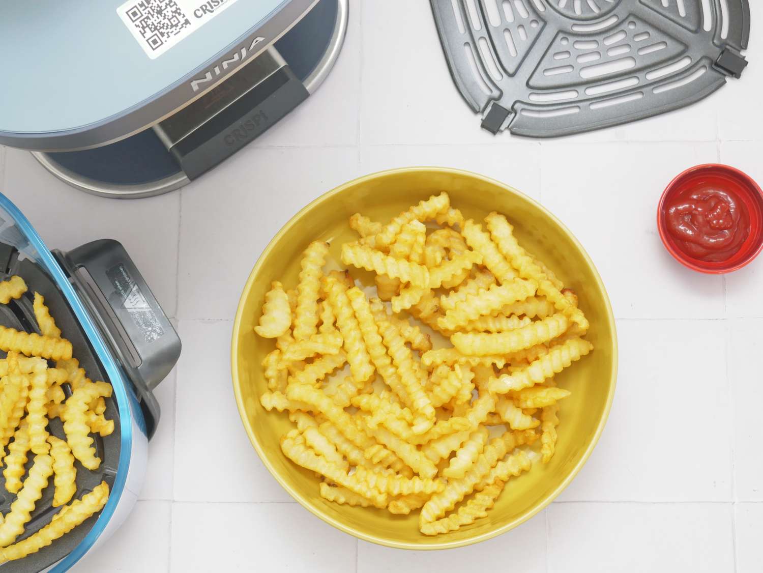 an overhead image of french fries in a bowl and the ninja crispi pro to the side