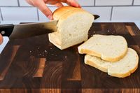 A hand slicing a loaf of bread with Tojiro F-687 Hand Made Bread Knife on a wooden cutting board