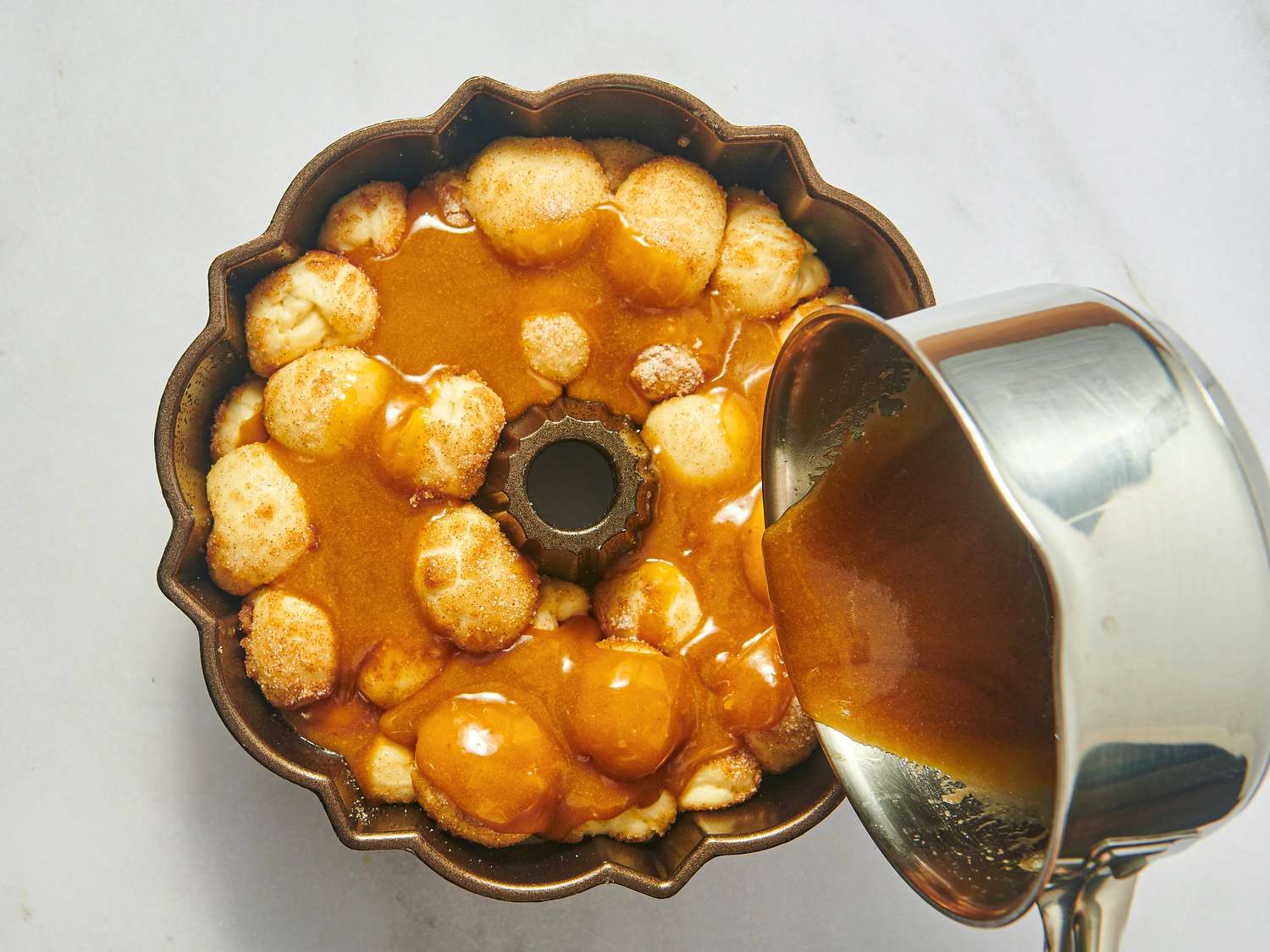Monkey bread in a bundt pan with caramel sauce being poured on top