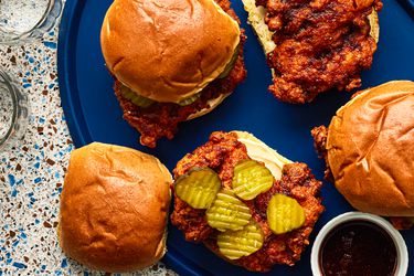 Overhead view of four Nashville hot chicken sandwiches, two open face, one with pickles on a blue serving platter.