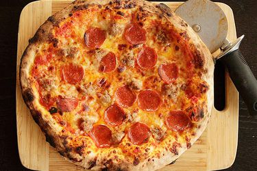 A homemade New York-style pepperoni pizza on a cutting board with a pizza wheel.