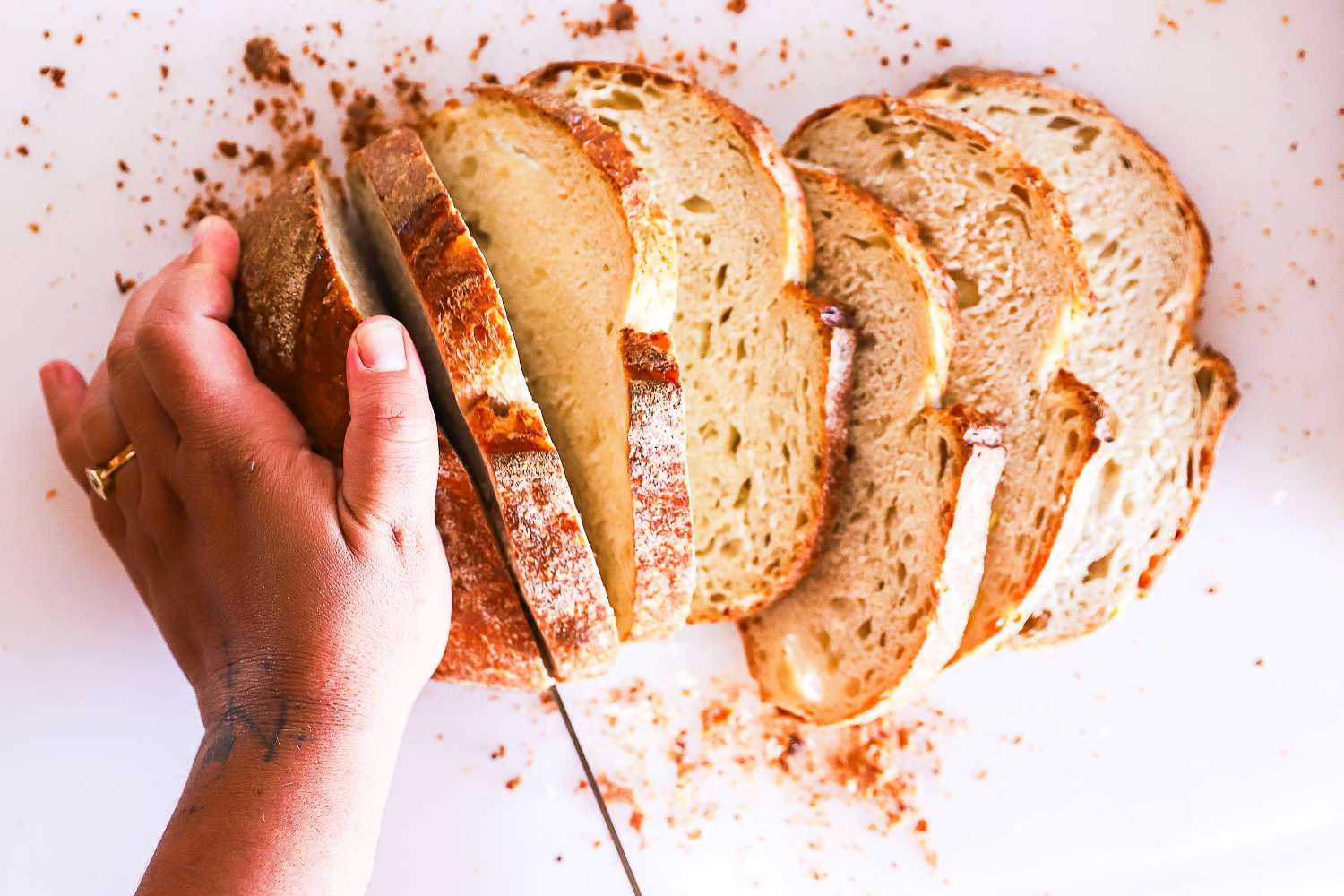 A hand slicing a loaf of bread with a Shun knife on a cutting surface