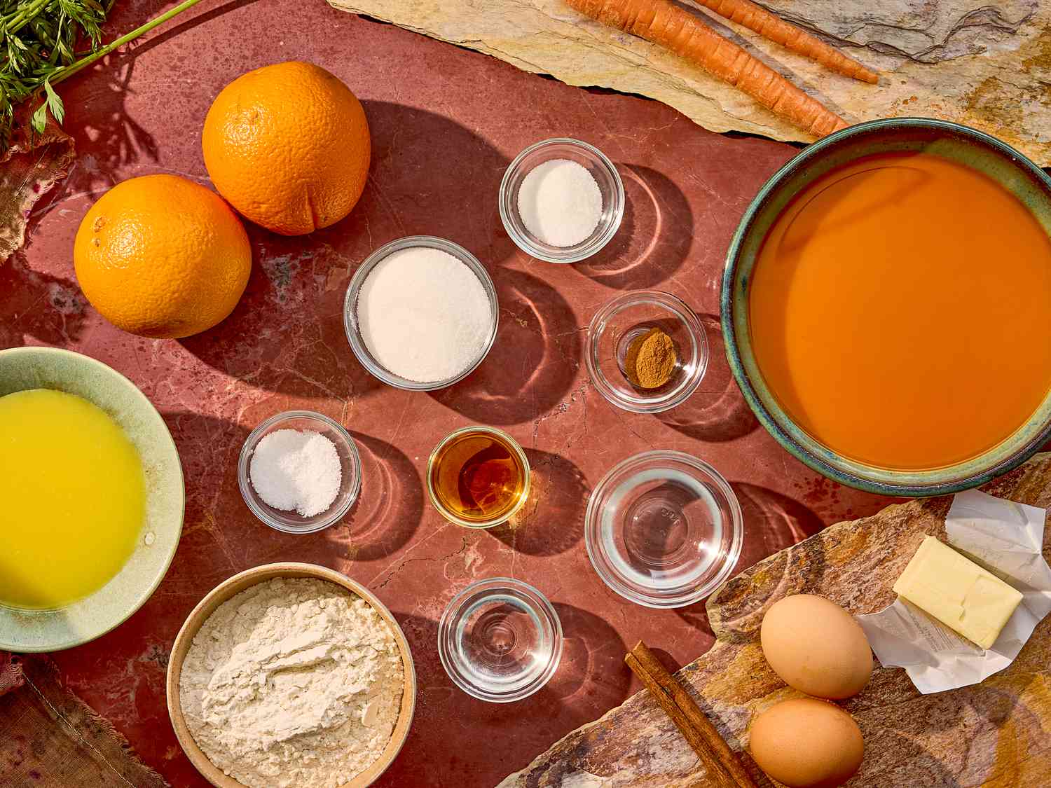 Ingredients arranged for a carrot crepes Suzette recipe, including oranges, eggs, flour, butter, and a small bowl of carrot juice