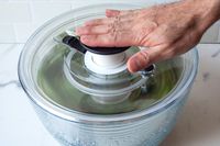 a person pumping the oxo glass salad spinner