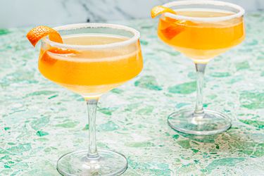 Two sidecar cocktails in stemmed cocktail glasses with sugared rims and an orange peel garnish 