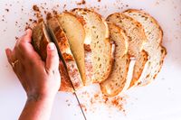 A hand slicing a loaf of bread with a Shun knife on a cutting surface