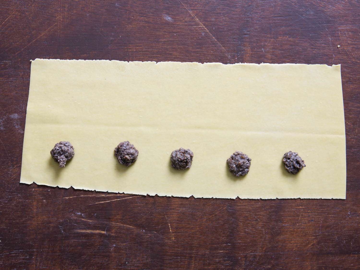 Scoops of mushroom filling has been evenly spaced on the bottom half of the creased pasta sheet.