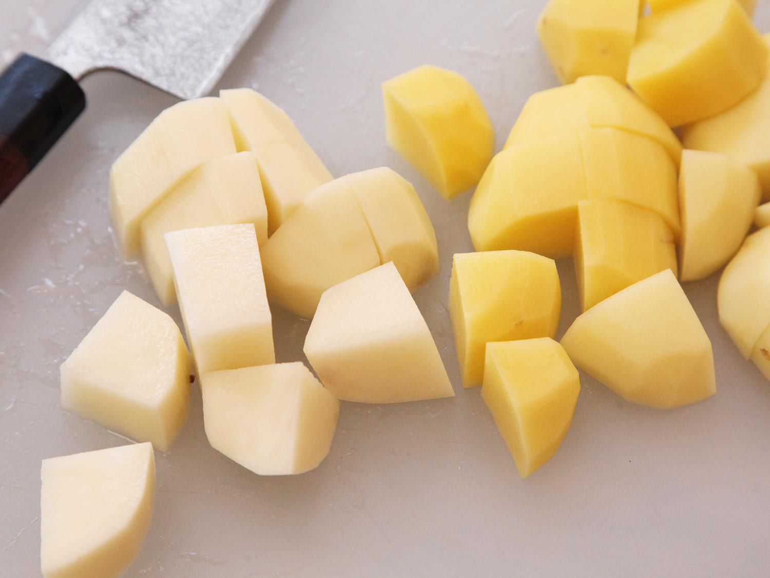 Chopped russet potatoes (left) and Yukon golden potatoes (right) on white cutting board.