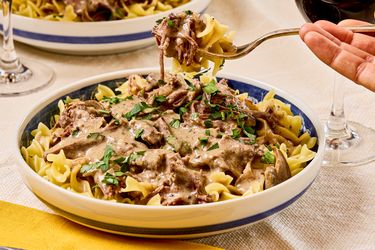 A fork lifting a portion of beef stroganoff served over egg noodles garnished with parsley