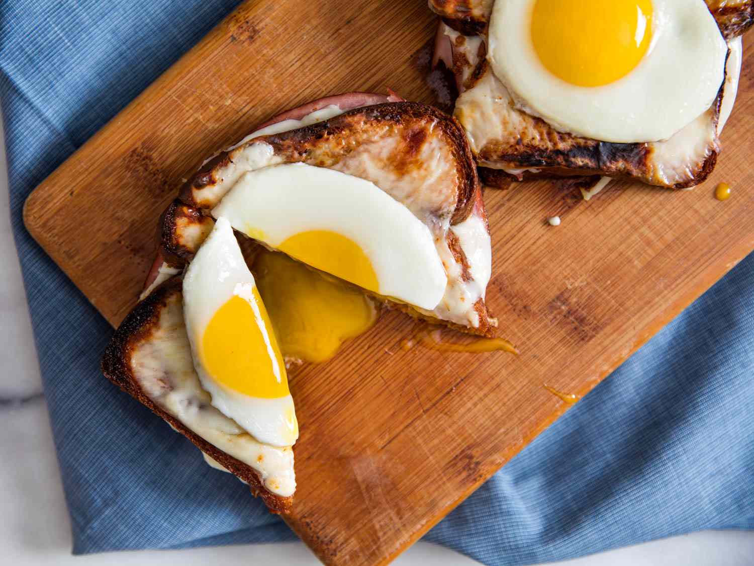 Two croque madame sandwiches with sunny side eggs on top. One is split in half with a golden yolk running out.