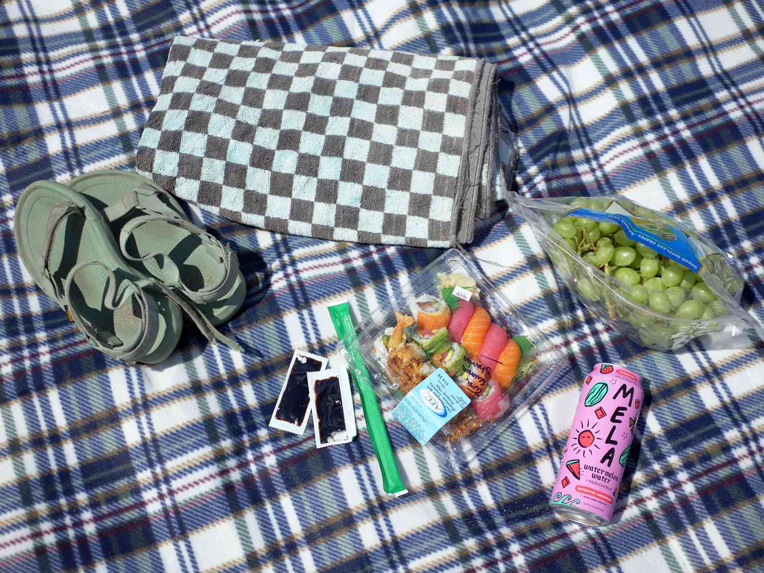 a picnic of sushi, grapes, and watermelon water on a fleece picnic blanket