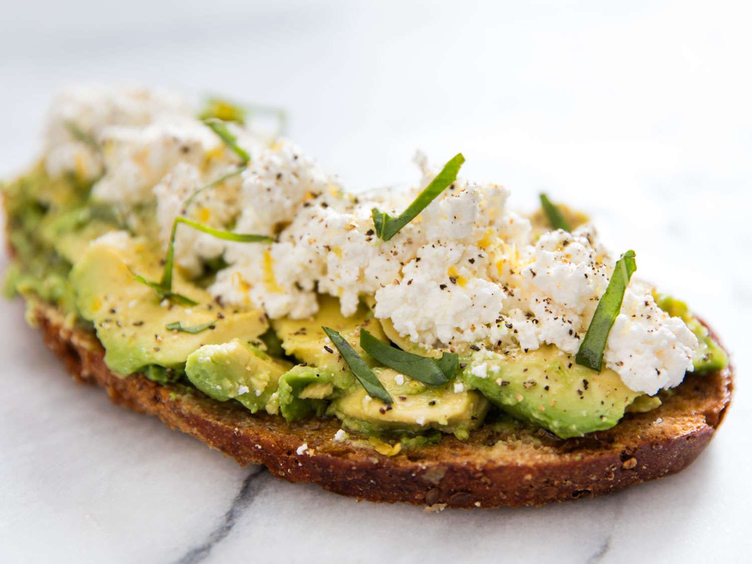 Avocado toast topped with homemade ricotta, chiffonade of basil, black pepper, and a drizzle of olive oil.