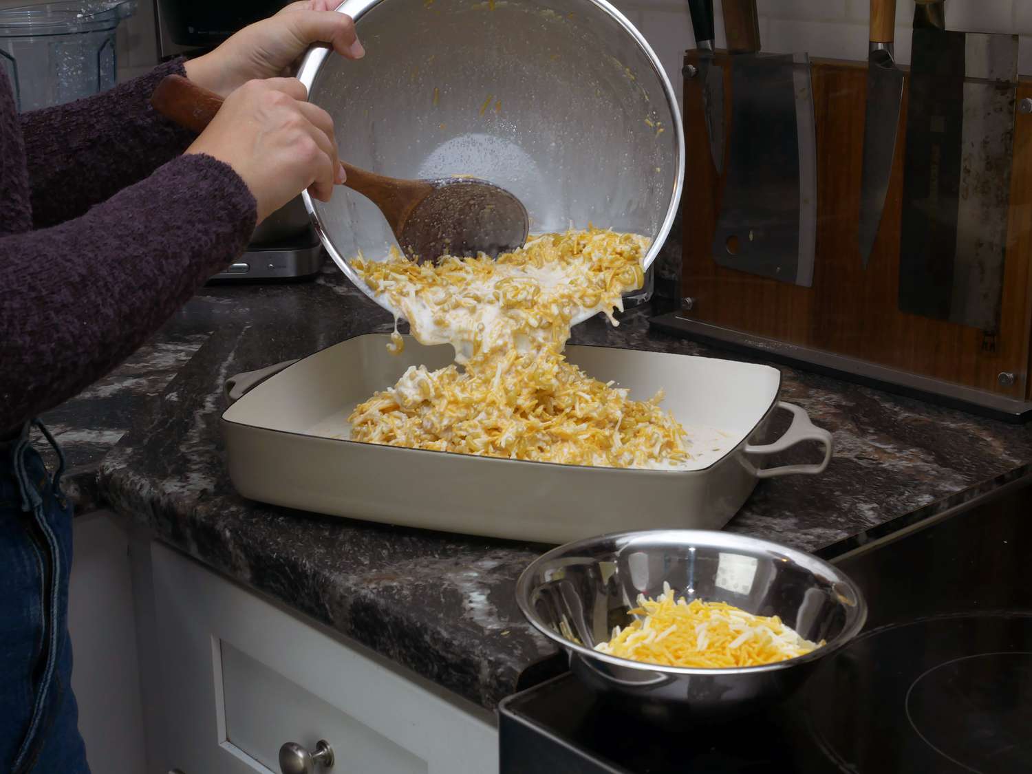 a person pouring macaroni and cheese mixture into casserole dish on counter