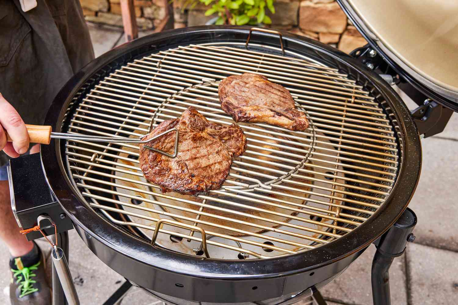 A person cooks meat inside the Weber 18201001 Summit Kamado E6 Charcoal Grill