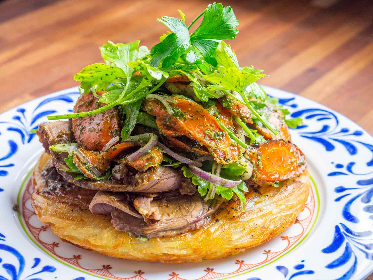 A potato cake topped with thinly sliced roasted lamb and a roasted carrot salad with fennel frond pesto