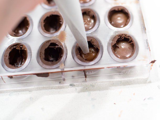 Using a piping bag to pipe a solid filling into bonbon shells within a mold.