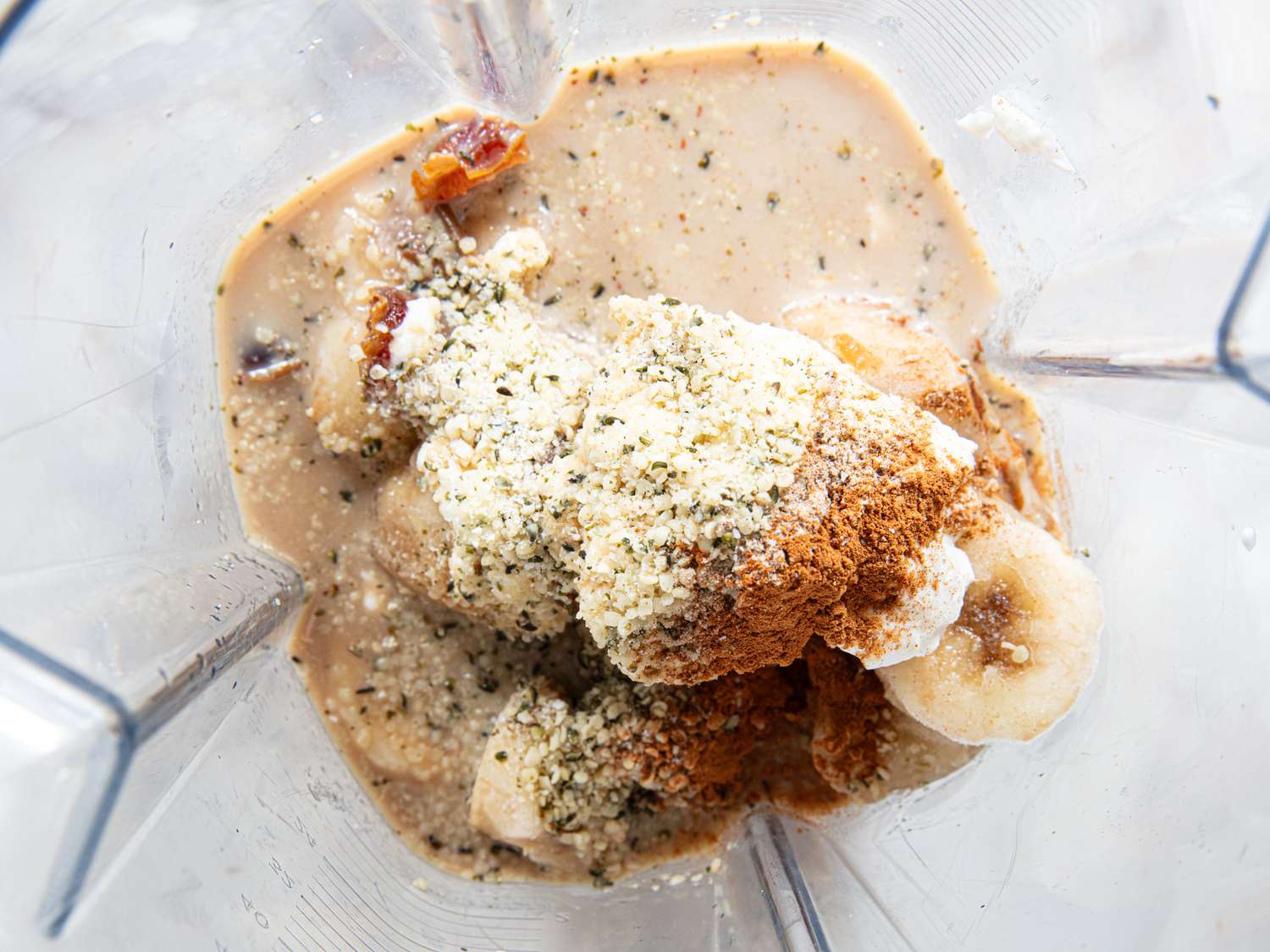 Ingredients for a banana smoothie including banana slices spices and seeds in a blender container