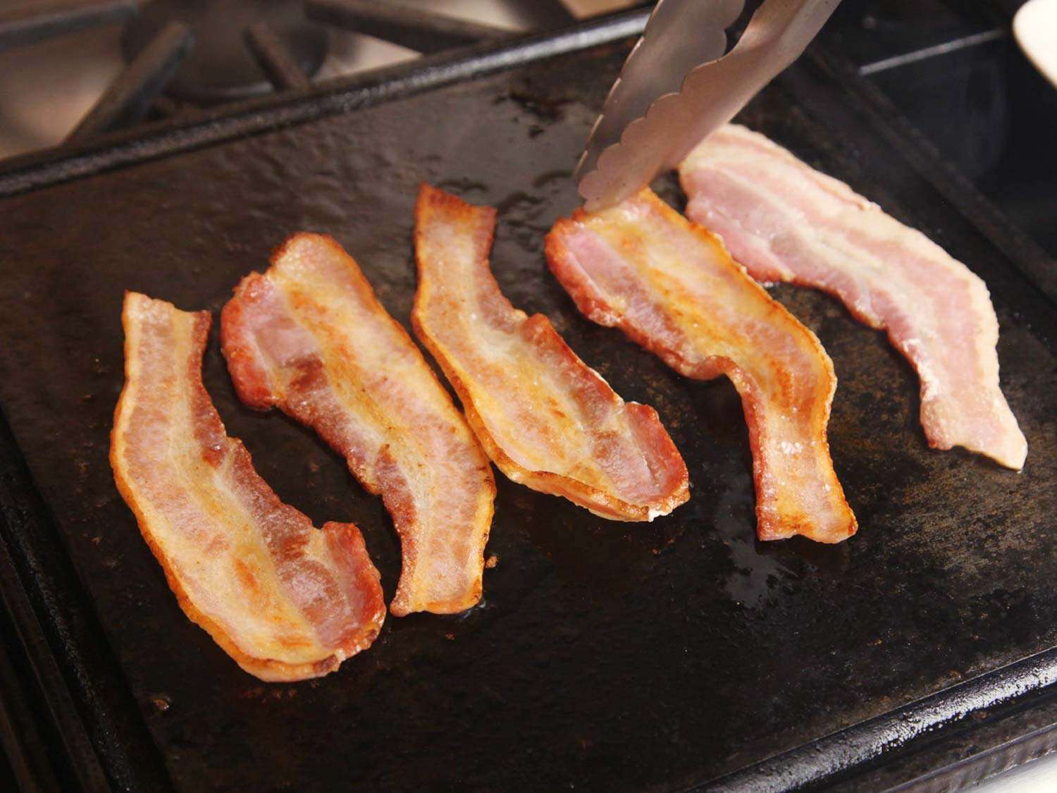 The cooked bacon getting crisped up on a griddle.