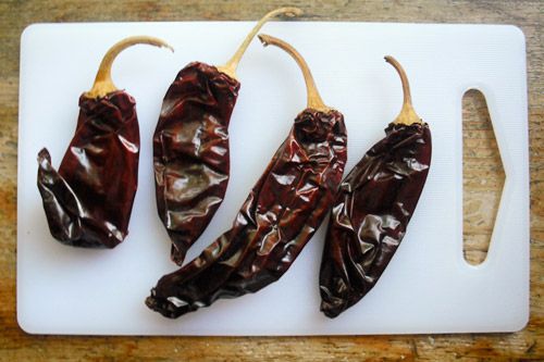 Four Chile guajillo resting on a plastic cutting board.