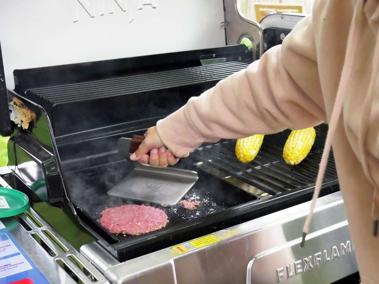 a person using a grill press to smash burgers on a griddle in a grill