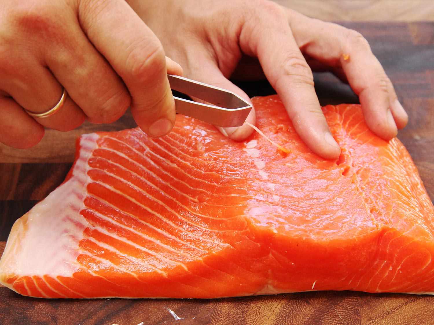Close up photo showing using fish tweezers to remove pin bones from large salmon fillet.