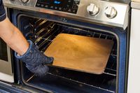 A person wearing an oven mitt and removing a baking steel from the oven.