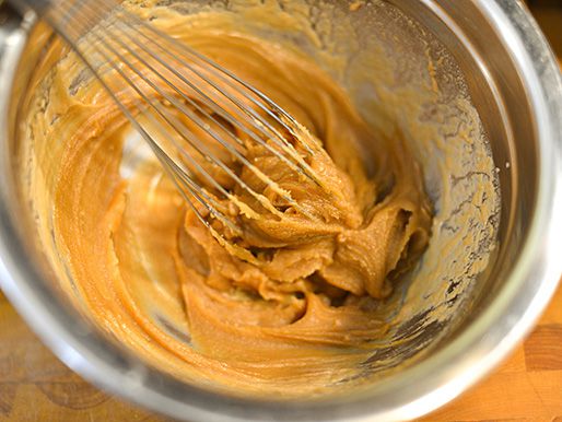 Whisking together peanut butter and hot water in a metal bowl.