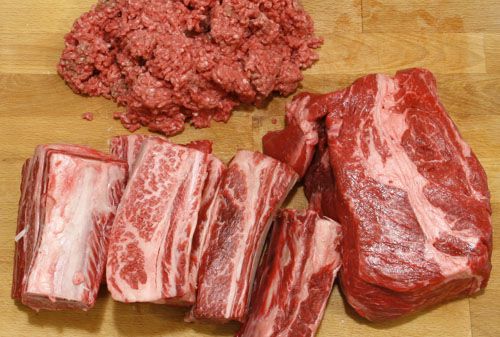 Ground chuck, chuck roast, and beef short ribs on a wooden cutting board to test for chili.