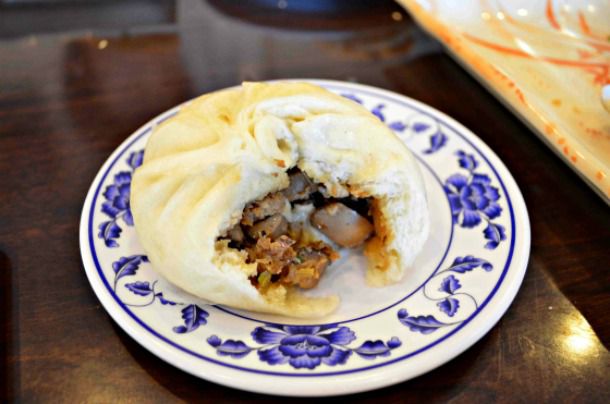 A mushroom pork bun served on a plate. A bite has been taken from the bun to reveal the pork-mushroom filling.