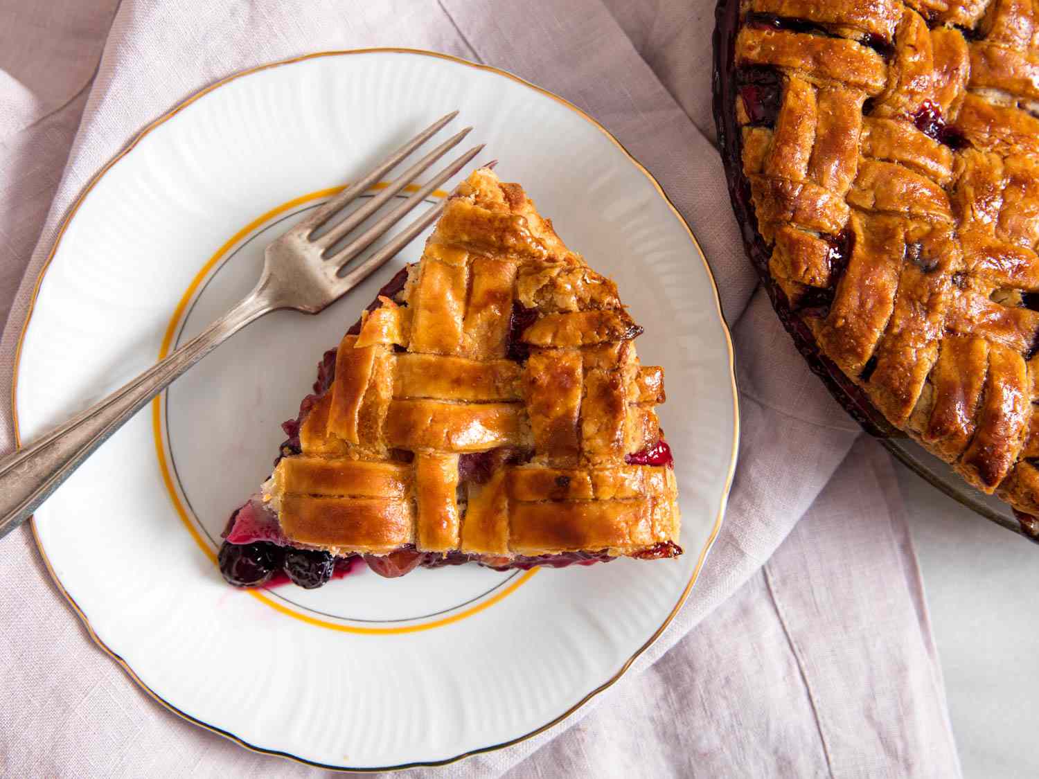 Overhead shot of a generous slice of fruit pie on a plate, flanked by a fork. The rest of the pie is nearby, mostly out of frame.