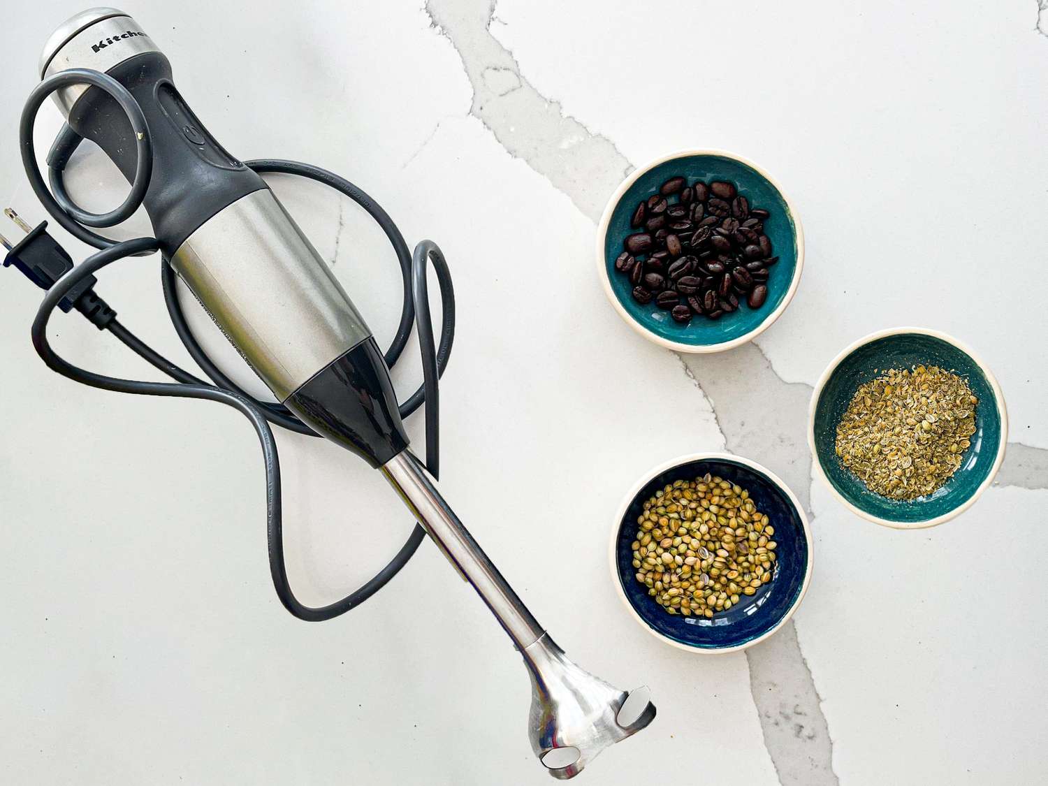 Immersion blender next to three bowls of coffee beans and spices