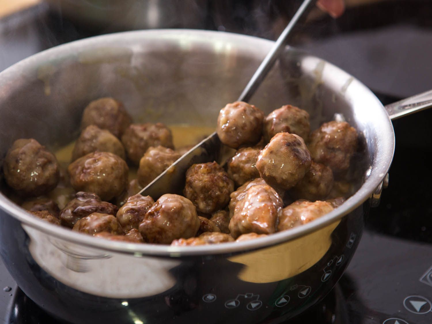 Golden brown Swedish meatballs being mixed into gravy.