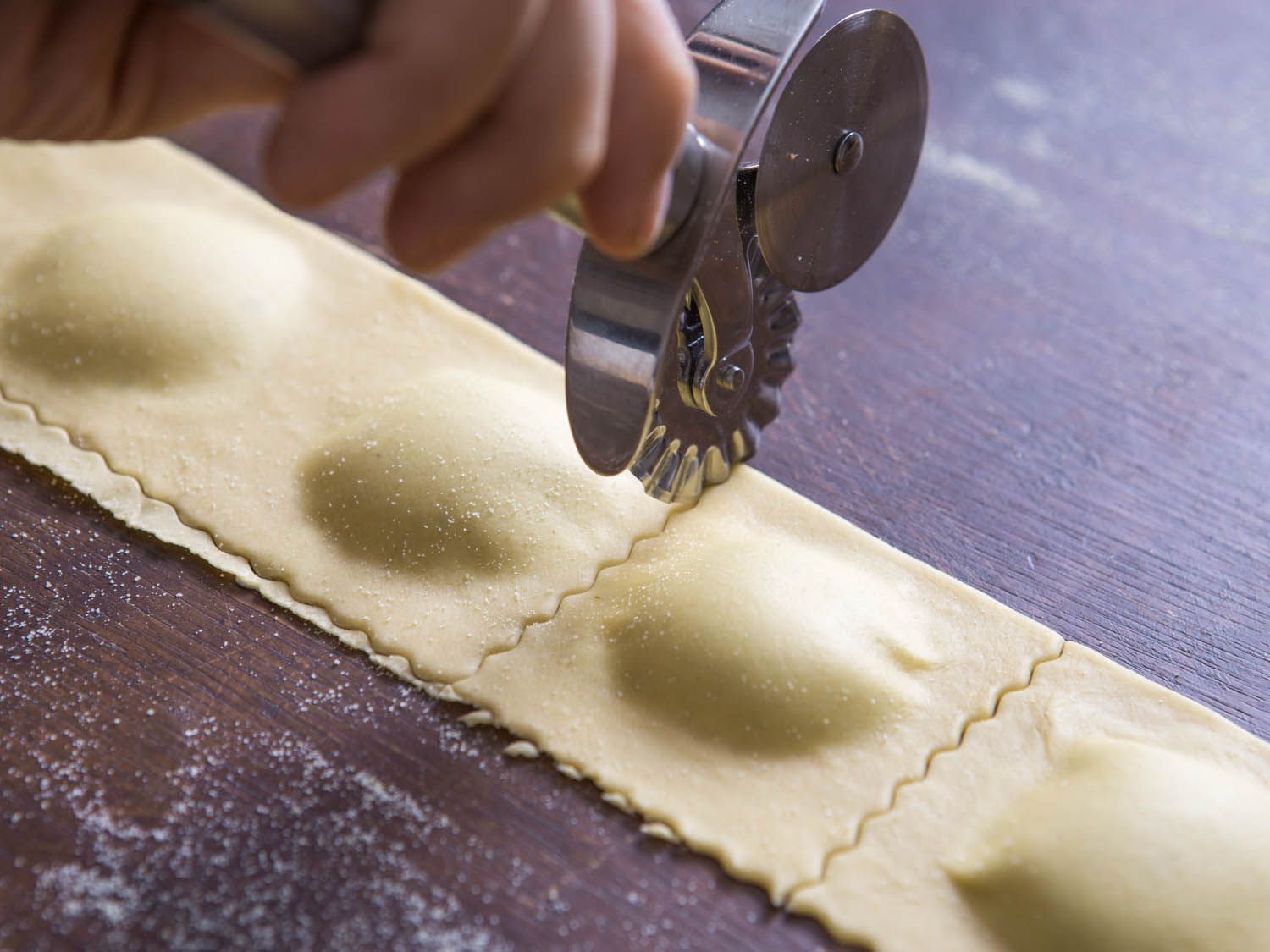 Ravioli being cut with a fluted pasta wheel cutter.