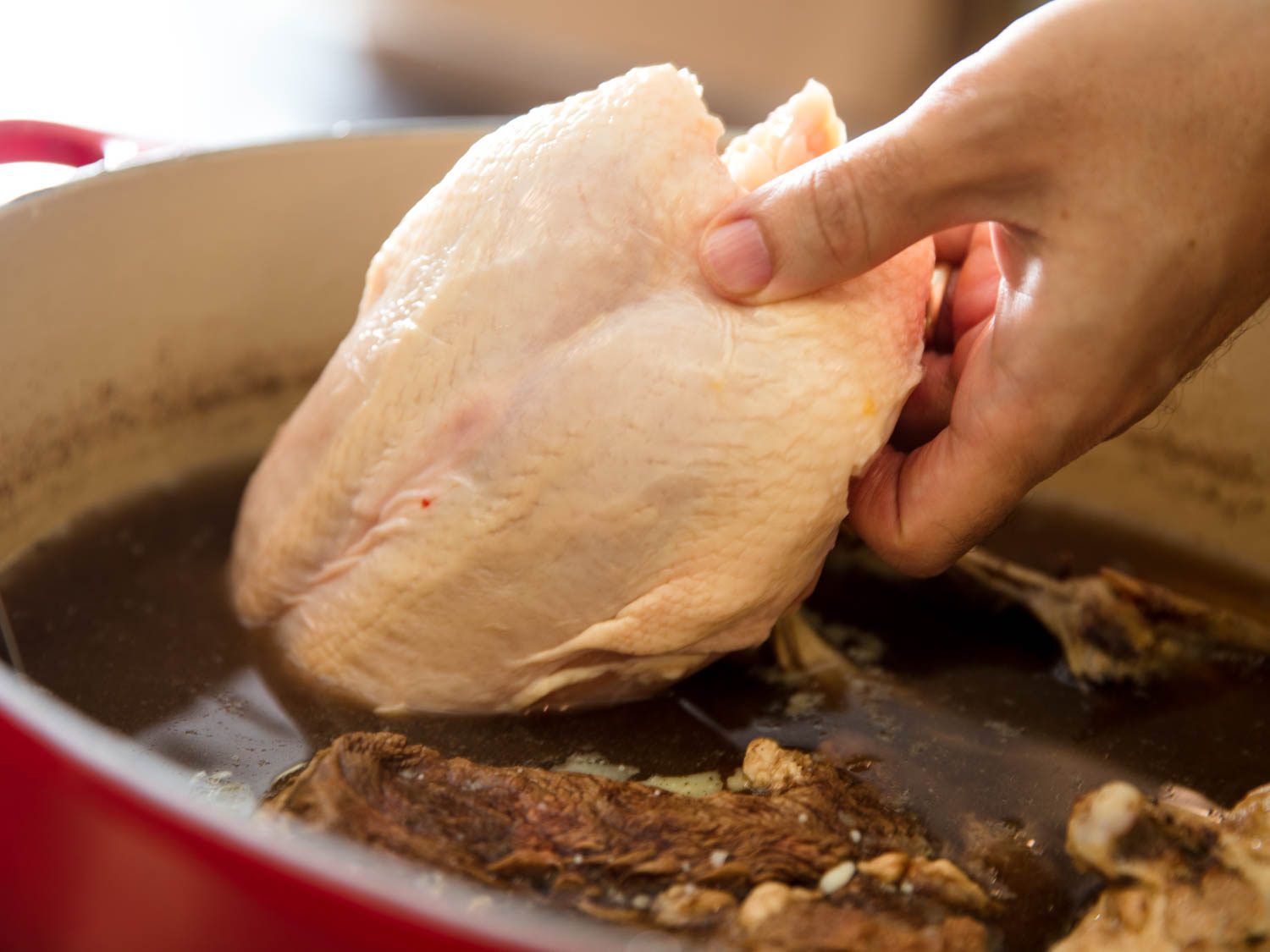 chicken breast being lowered into a pot of bollito misto