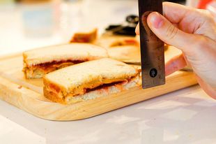 Measuring the thickness of a cut peanut butter and jelly sandwich on a wood cutting board. 