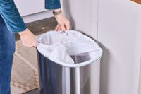 A person places a trash bag into the iTouchless 13-Gallon Oval Stainless Steel Sensor Trash Can
