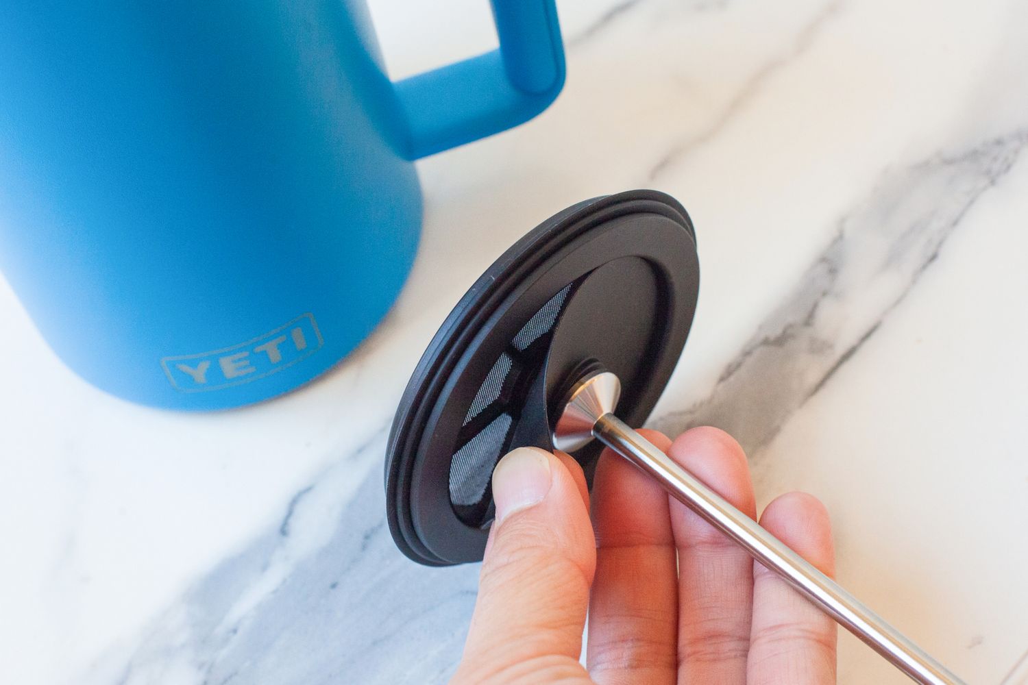 A hand holding the press attachment of the Coffee being poured from the Yeti French Press into a mug