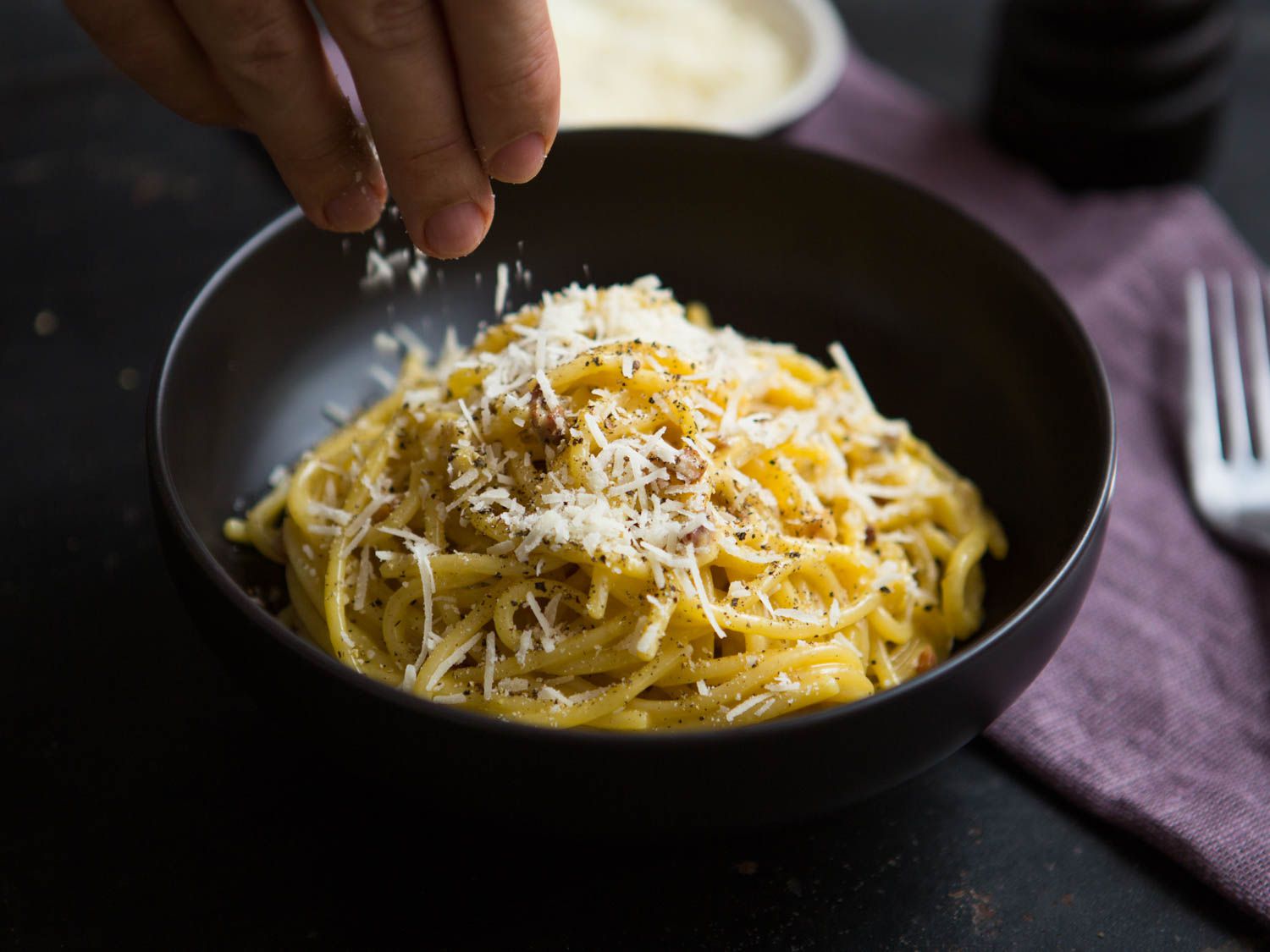 Sprinkling cheese on a bowl of spaghetti carbonara.