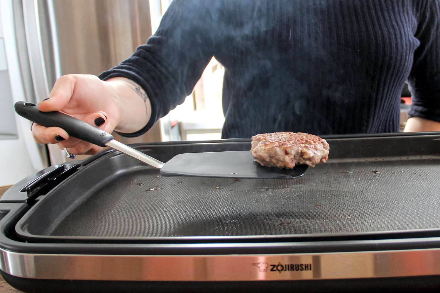 A person lifts a burger with a nonstick food turner.